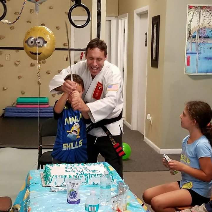An instructor helps a birthday child cut the cake with a sword