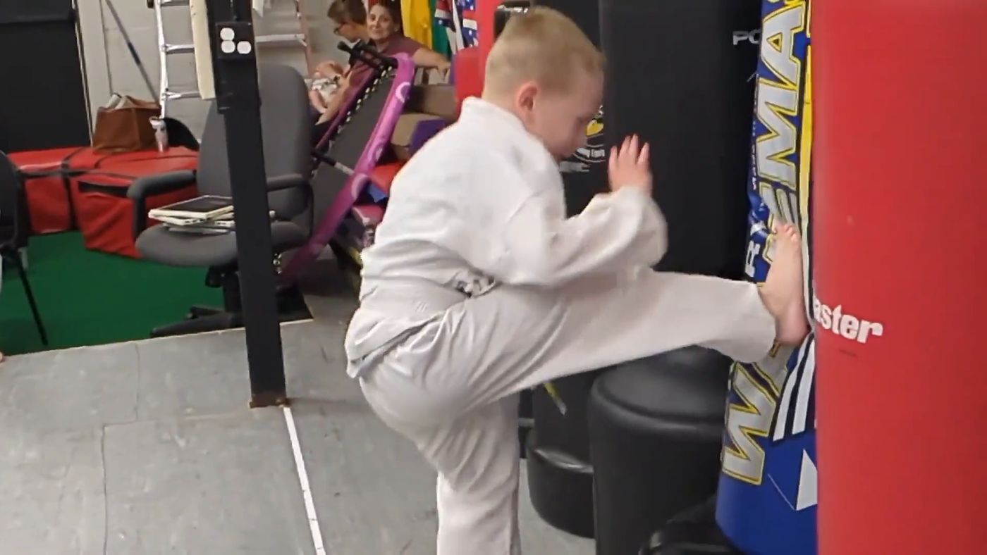 A student delivers a high kick to a heavy bag