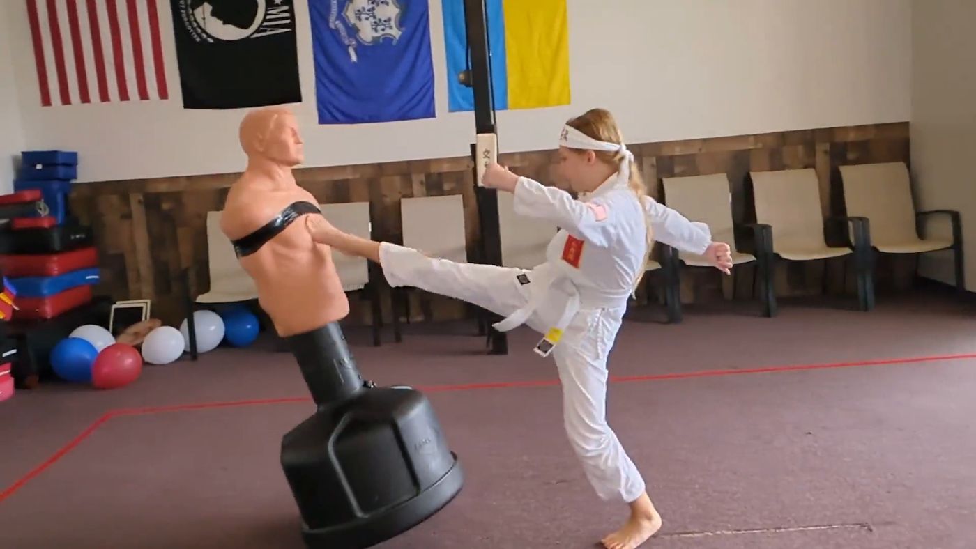 A young student in a white gi kicks a training dummy