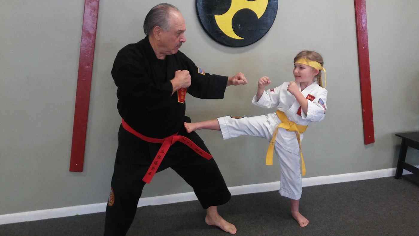 An instructor in a black gi works with a young student in the dojo